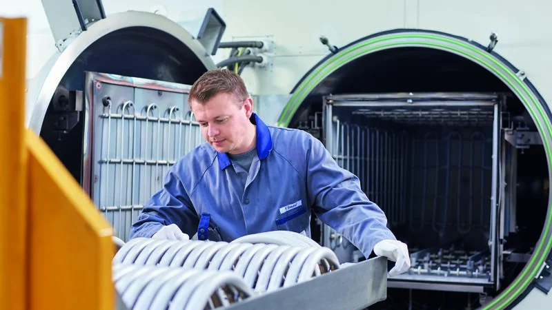 Worker loads a tray of metal components into the open chamber of a large high vacuum brazing furnace.